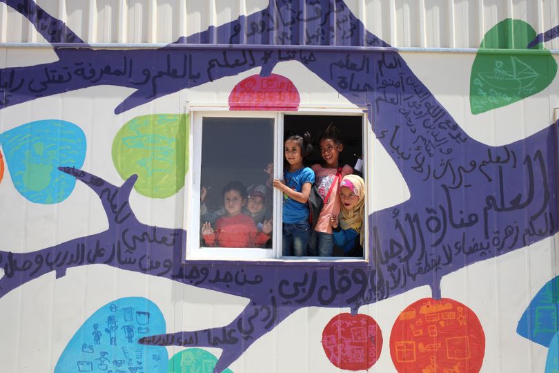 Syrian refugee children peer from the window of their classroom, newly decorated with a mural, at Zaatari refugee camp, near the Syrian border, in Mafraq, Jordan, Tuesday, July 23, 2013.  Several writings in Arabic can be read on the mural, made up of old sayings and poetry that encourage the people to seek knowledge. Most of the trailers and tents match the beige color of the swirling sand surrounding the Zaatari refugee camp, home to about 120,000 Syrians who fled the nearly three-year war still gripping the nation. Slowly though, that's changing with the help of a U.S.-based artist who is leading children haunted by the conflict to paint buildings and walls at the crowded camp with murals expressing their lives and hopes. (Mohammad Hannon / Associated Press)