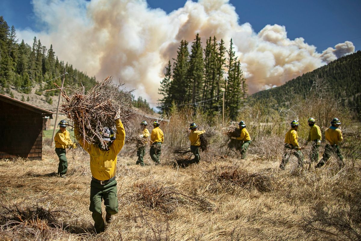 Firefighters with Structure Group 4 clear brush and debris away from cabins along Highway 518 near the Taos County line in New Mexico, May 13, 2022, while fire rages over the nearby ridge.  (Jim Weber)