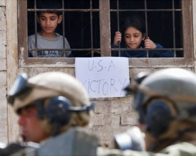 In this April 16, 2003, AP file photo, Iraqi children look down from their window where they hung a pro-American sign while U.S. forces guard an area near a Baghdad bank. (AP Photo/Hussein Malla file)