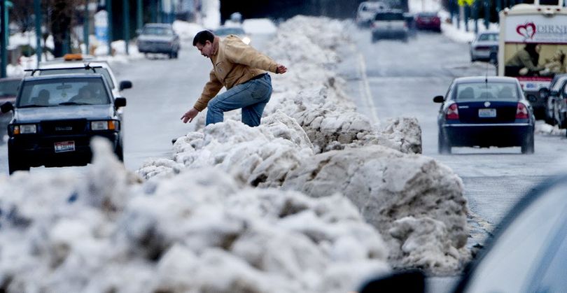 A pedestrian climbs over the three-foot snow berms in the turning lanes of Sherman Avenue in downtown Coeur d'Alene on Tuesday. The City of Coeur d'Alene will begin removal of the berms using a snow blower and dump truck this evening. KATHY PLONKA kathypl@spokesman.com 