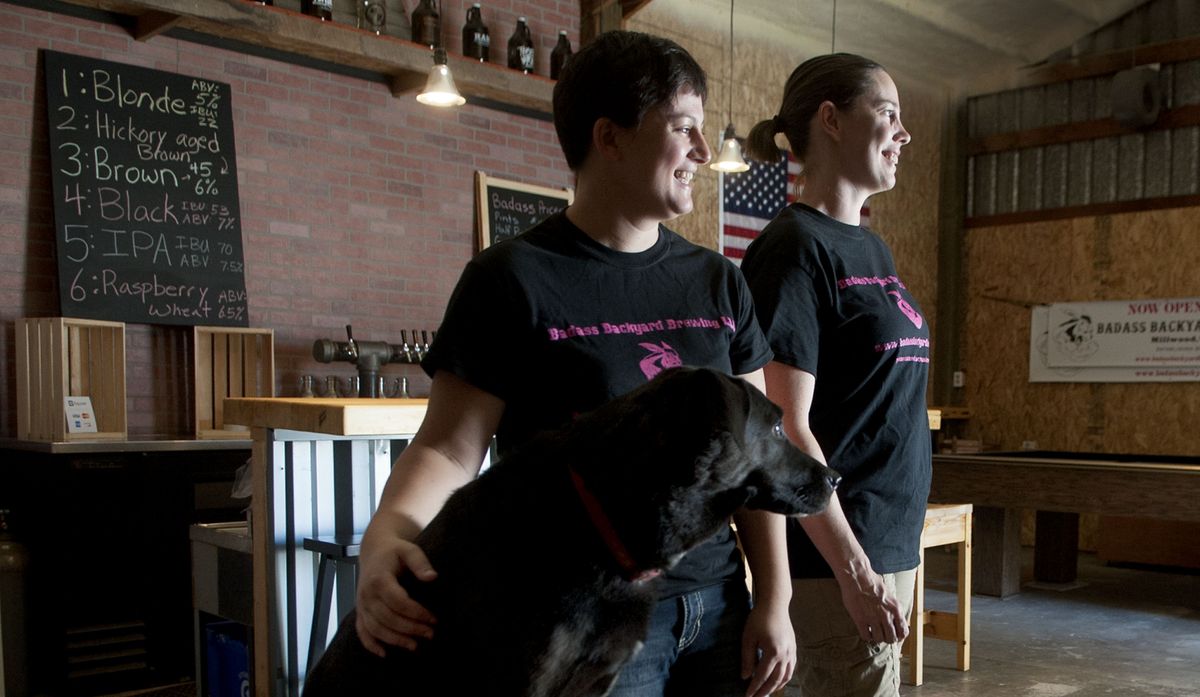 Badass Backyard Brewing owner Charlene Honcik, left, and Kendra Wiiest are joined by Jackson the black Lab in the Millwood brewery. “He’s our motivator,” Honcik says of Jackson, also pictured below. (Kathy Plonka)