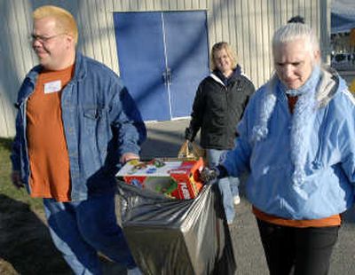 
Volunteers from the Coeur d'Alene Casino, Ray LaSarte and Melinda Helms, carry a bag of toys to the parking lot for Tonya Stampfl on the opening day of the Christmas Bureau at the Spokane County Fair and Expo Center.
 (The Spokesman-Review)