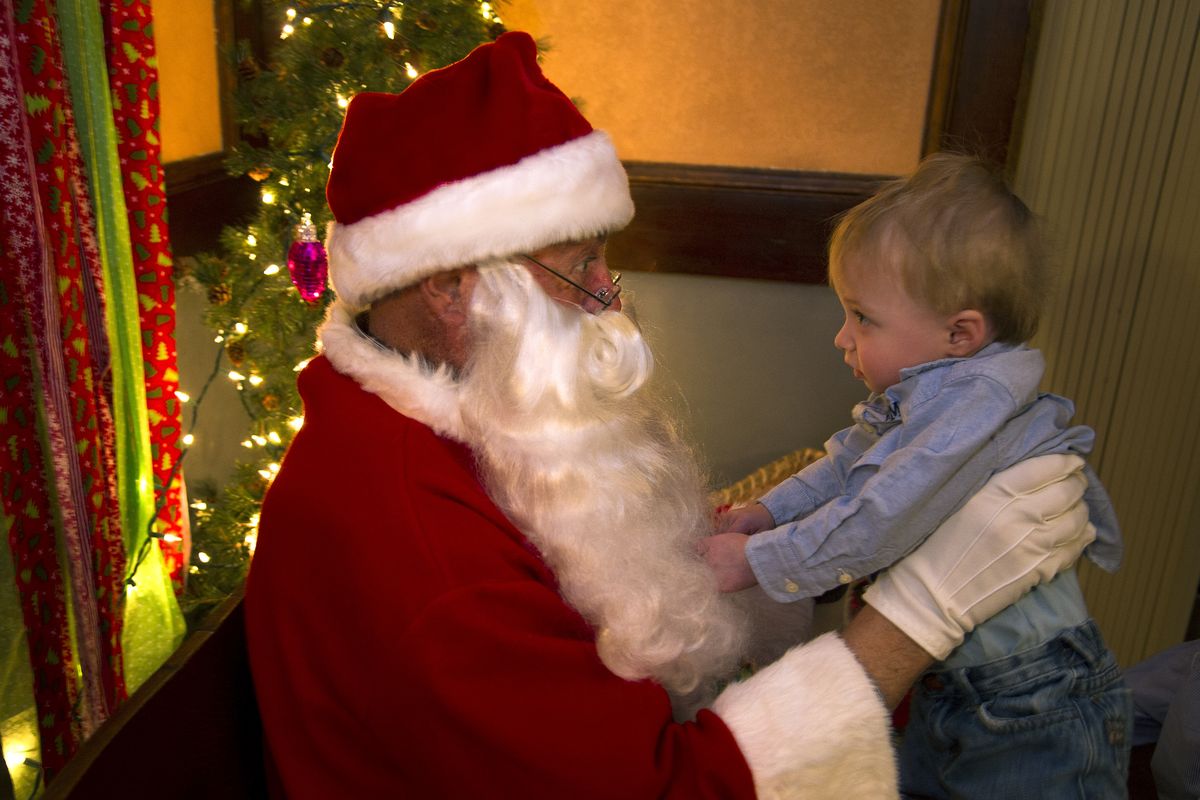 Hudson McLaughlin, 1, meets Santa (Mike Rubert) at The Harvester Restaurant in Spangle, Wash., earlier this month. Rubert has played Santa in Spangle for four years and has always sported his own beard. This year, however, he’s recovering from cancer surgery and has a clean-shaven face. (Colin Mulvany)