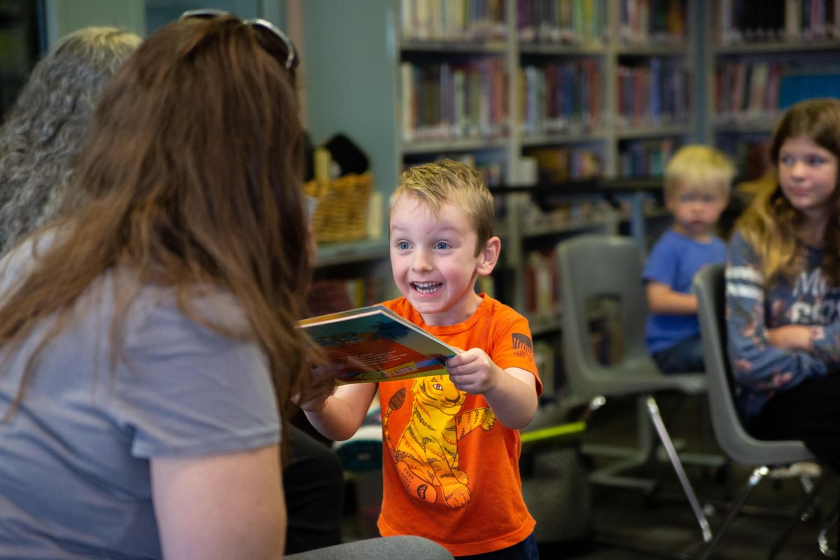 Mason Murphy, 5, excitedly shows off a book about dinosaurs that he received in a contest from author Kelly Milner Halls, who wrote the book, on June 29, 2018. Mason was one of about a dozen children who attended a summer reading event at Evergreen Elementary School under a districtwide network of programs put on by Mead School District. (Libby Kamrowski / The Spokesman-Review)