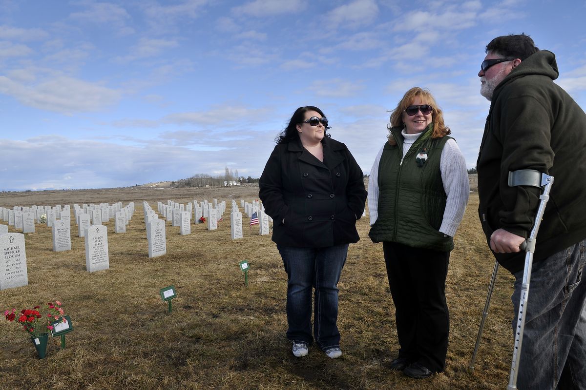 From left, Katy O’Grady, Cathy Dodson and Mike Dodson stand by the grave of Kevin O’Grady, the father and brother-in-law of the three, on Sunday at the Washington State Veterans Cemetery near Medical Lake. After O’Grady died during treatment for lymphoma, his cremated remains were lost in the mail. His family held his service as his remains traversed the country. (Jesse Tinsley)