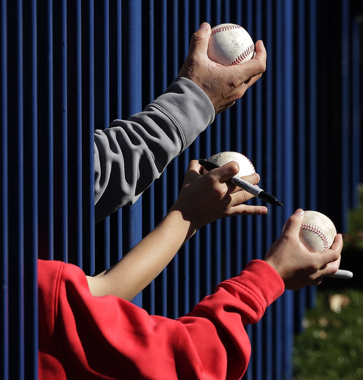 Fans armed for autographs reach through a fence trying to entice Mariners players to sign Monday. (Associated Press)