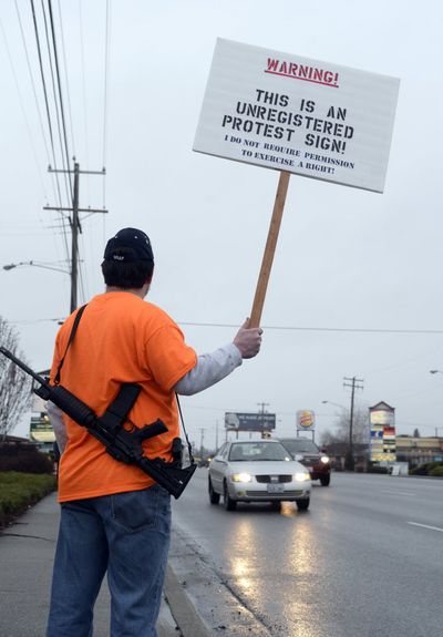 Sam Palmer wears his AR15 and holds a sign along Sprague Ave. Saturday, Dec. 20, 2014 during a protest by self-labeled 