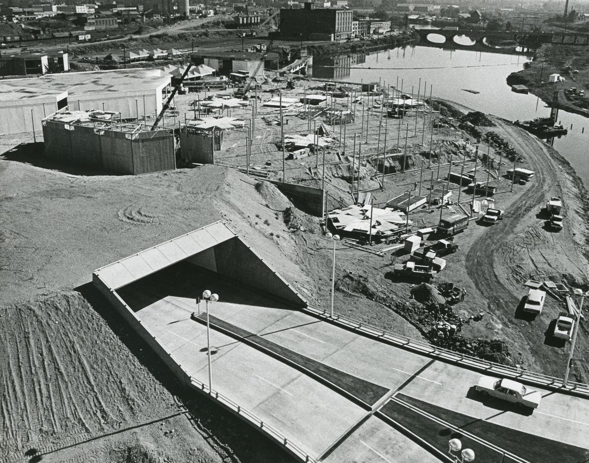 As seen from the downtown clock tower, the Y-shaped Washington-Stevens Street bridge connects to a new tunnel through Havermale Island. Construction of pavilions for the world’s fair cover the landscape of Havermale Island, long an industrial site covered with train tracks, warehouses and other service building. Dirt was banked up and over the tunnel to create a park-like natural area for attendees of Expo ’74. 