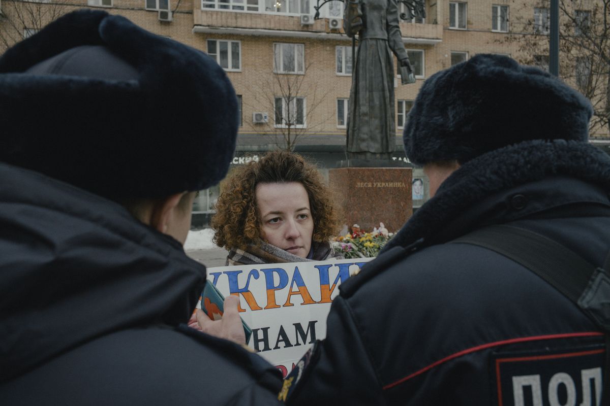 The police approach Katja, 26, who was protesting at the impromptu memorial for the Ukrainian writer Lesya Ukrainka in Moscow, on Jan. 19, 2023, in memoriam to those killed by a Russian missile strike in Dnipro, Ukraine. For more than half an hour on Friday, Katya stood in front of the statue with the sign; she was later detained by the police.    (Nanna Heitmann/The New York Times)