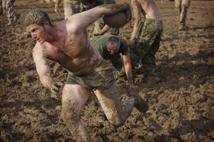 A United States Army soldier runs with the ball as United States Marines from the 2nd MEB, 4th Light Armored Reconnaissance Battalion try to tackle while playing a game of mud football following a rain storm at their base in Khan Neshin, in the volatile Helmand province of southern Afghanistan, Wednesday, Dec. 9, 2009. (Kevin Frayer / Associated Press)