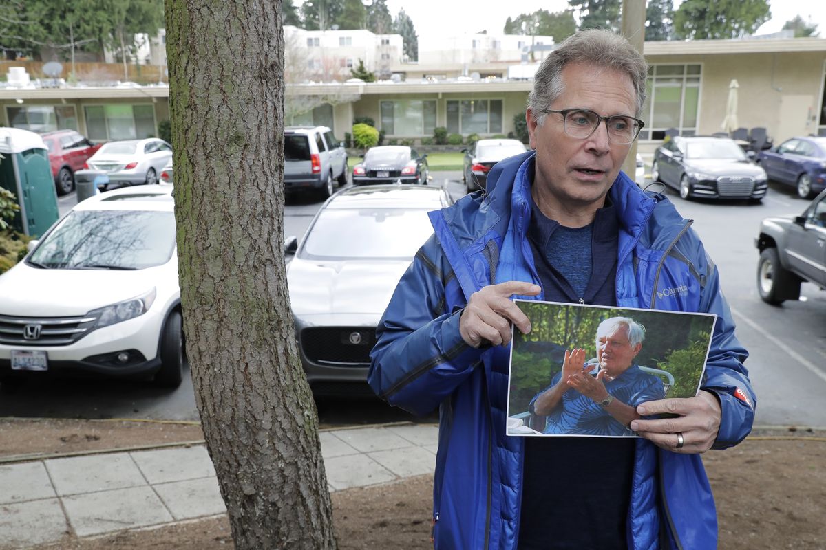 FILE - In this March 12, 2020, file photo, Scott Sedlacek poses while holding a photo of his father, Chuck, outside Life Care Center in Kirkland, Wash., near Seattle. Sedlacek battled having COVID-19 while his father also fought the virus and was under care in the facility. Both have since recovered. Hearing of President Donald Trump
