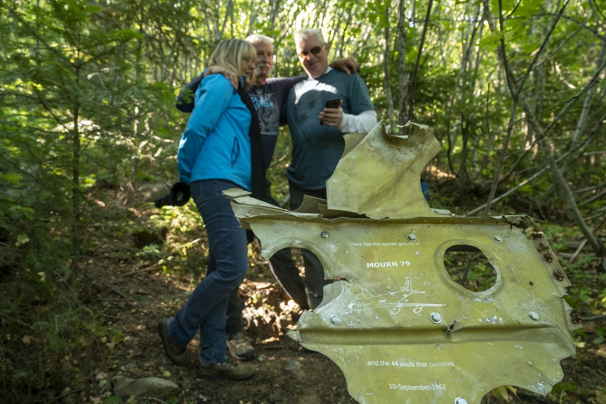 Talking to their mother on a cellphone, siblings Grace Doumani, Gray Tillman and brother Randy Tillman, right, stand next to a makeshift memorial, made of an engraved piece of wreckage, on the spot in the Mount Spokane State Park where their father