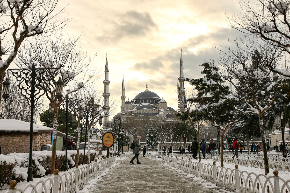 People walk in a snow-covered park with the iconic Haghia Sophia in the background at Istanbul, Tuesday, Jan. 25, 2022. Rescue crews in Istanbul and Athens on Tuesday cleared roads that had come to a standstill after a massive cold front and snowstorms hit much of Turkey and Greece, leaving countless people and vehicles in both cities stranded overnight in freezing conditions.  (Emrah Gurel)