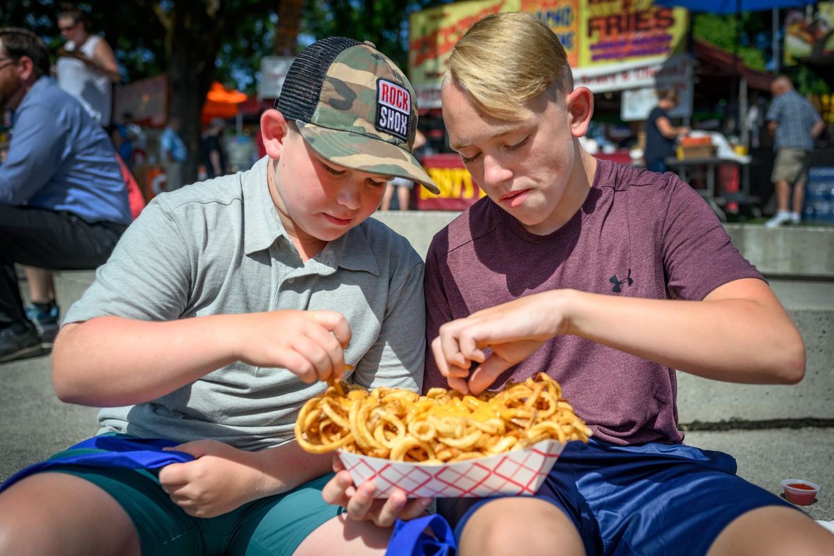 Brothers Oliver Hampson, 10, and Seth, 12, enjoy a “block of fries” during the opening day of the 2019 Pig Out in the Park in Riverfront Park.  (COLIN MULVANY)