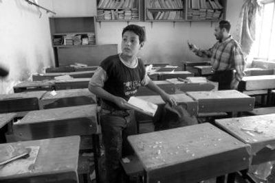 
A boy collects his books after a rocket landed at his schoolyard in eastern Baghdad on Tuesday. A Katushya rocket hit a basketball court at the  school, killing a 6-year-old boy and wounding 17 others. 
 (Associated Press / The Spokesman-Review)