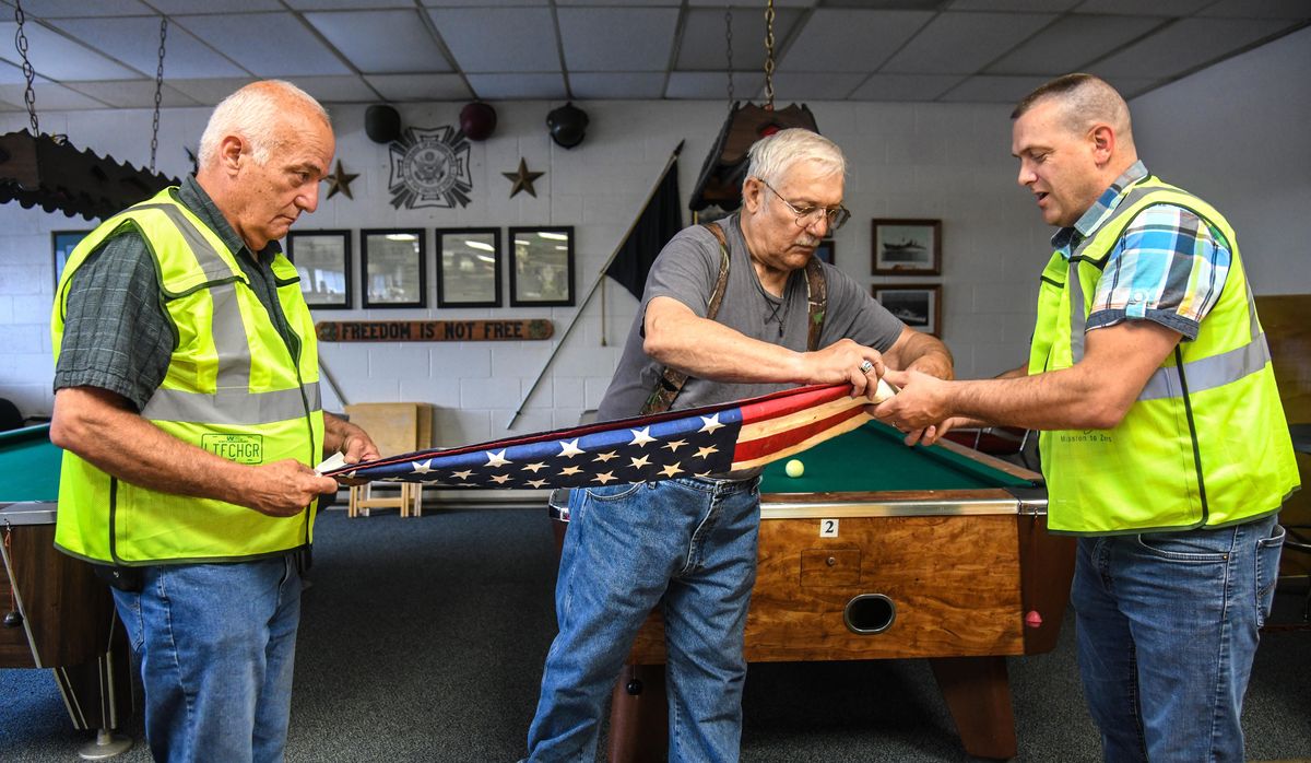 Tom Young, left, and Randy Colegrove, right, of Waste Management SMaRT Center, get an assist from VFW Post 51 Commander Sandy Judge as they fold an American flag that was pulled from the SMaRT Center pre-sort area. Young and Colegrove brought 27 flags to the VFW, Thursday, June 7, 2018, to be disposed of in a proper manor. (Dan Pelle / The Spokesman-Review)
