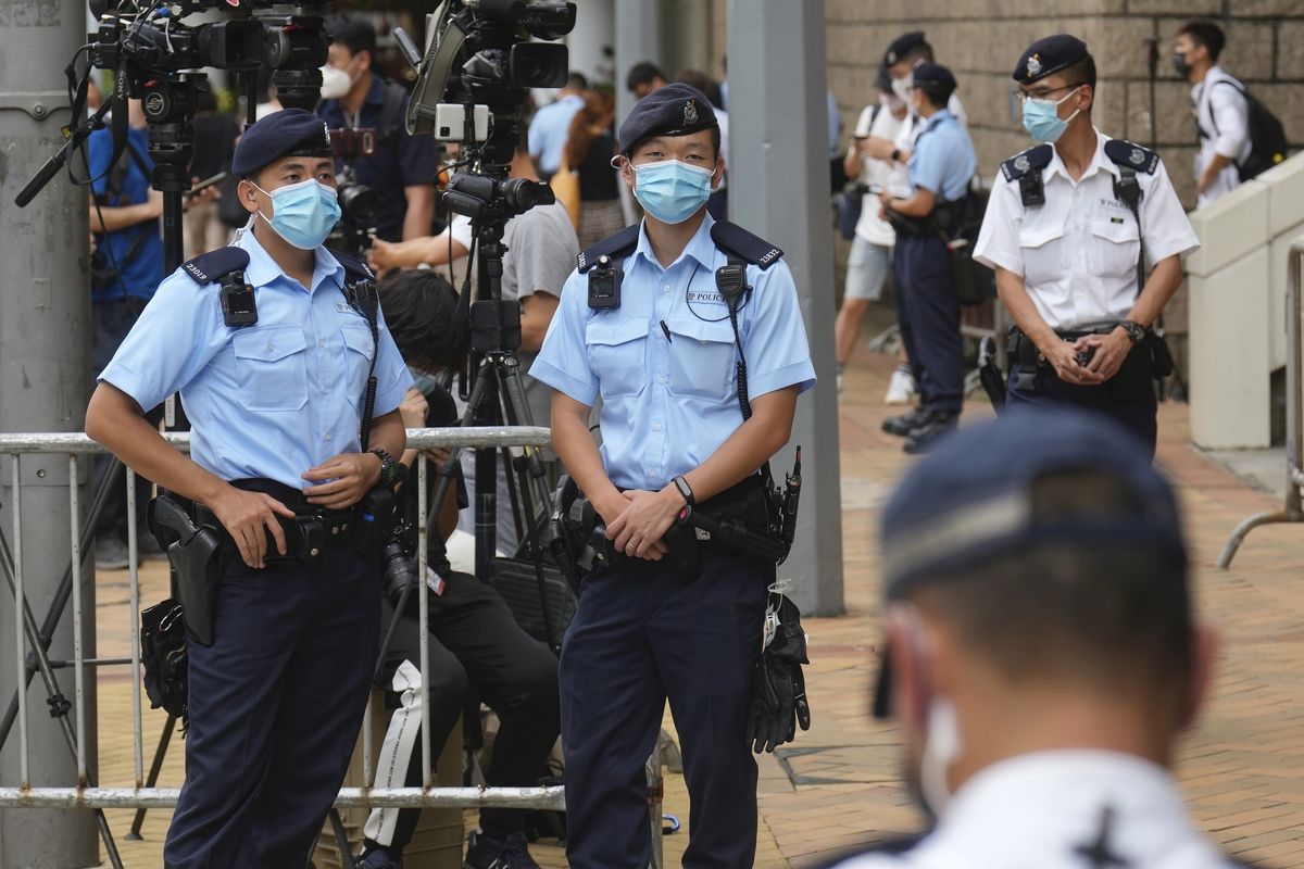 Police officers stand guard outside a court Friday, July 30, 2021, in Hong Kong, as a pro-democracy demonstrator Tong Ying-kit exits the court after his sentencing for the violation of a security law during a 2020 protest. Tong has been sentenced to nine years in prison in the closely watched first case under Hong Kong