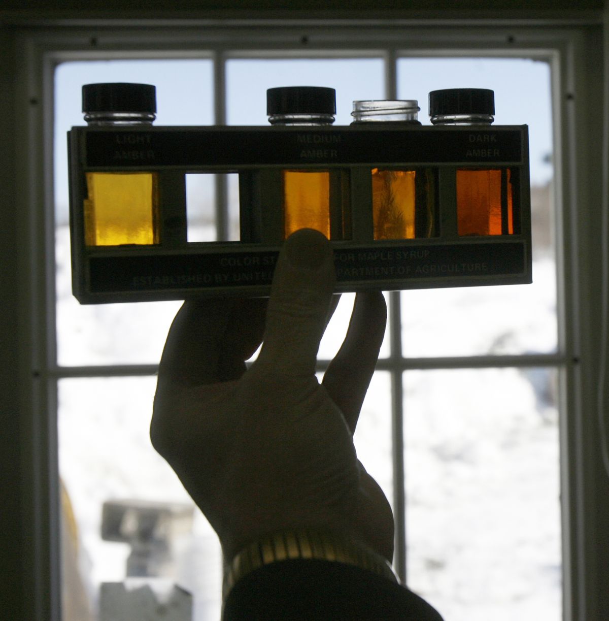 FILE-In this March 17, 2008, file photo, Henry Marckres holds a maple sample up for viewing in East Montpelier, Vt. Vermonters have grown accustomed to their �fancy� �amber� and �grade B� types of maple syrup but new consumers may not be so sweet on the terms. So the country�s largest producer of the pancake topping is thinking of doing away with those terms and adopting new international names with flavor descriptions to help consumers delineate between four different colored and flavored syrups and to match new worldwide terms. The four classifications would be golden color, delicate taste; amber color, rich taste; dark color, robust taste; and very dark color, strong taste. (Toby Talbot / Associated Press)