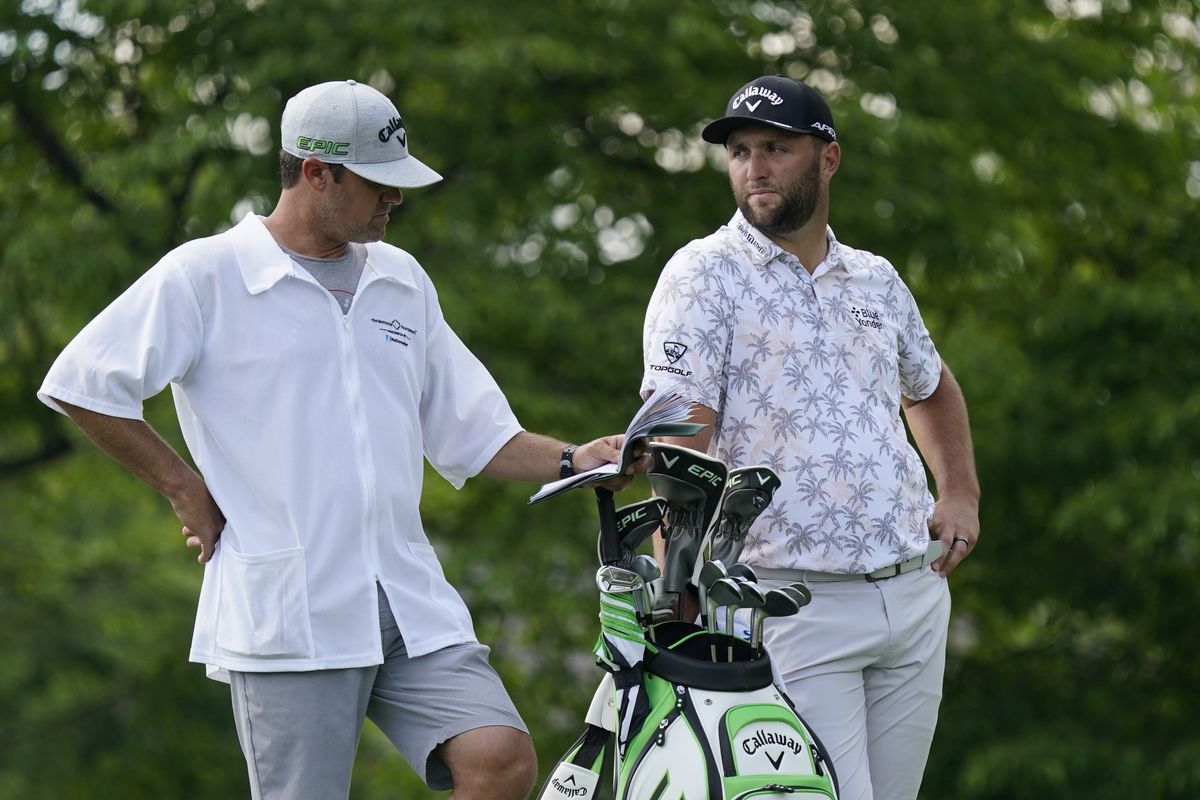 Jon Rahm talks with his caddie as he waits to hit on the 14th tee during the third round of the Memorial golf tournament, Saturday, June 5, 2021, in Dublin, Ohio. Rahm was later notified he tested positive for the coronavirus, knocking him out of the tournament.  (Darron Cummings)