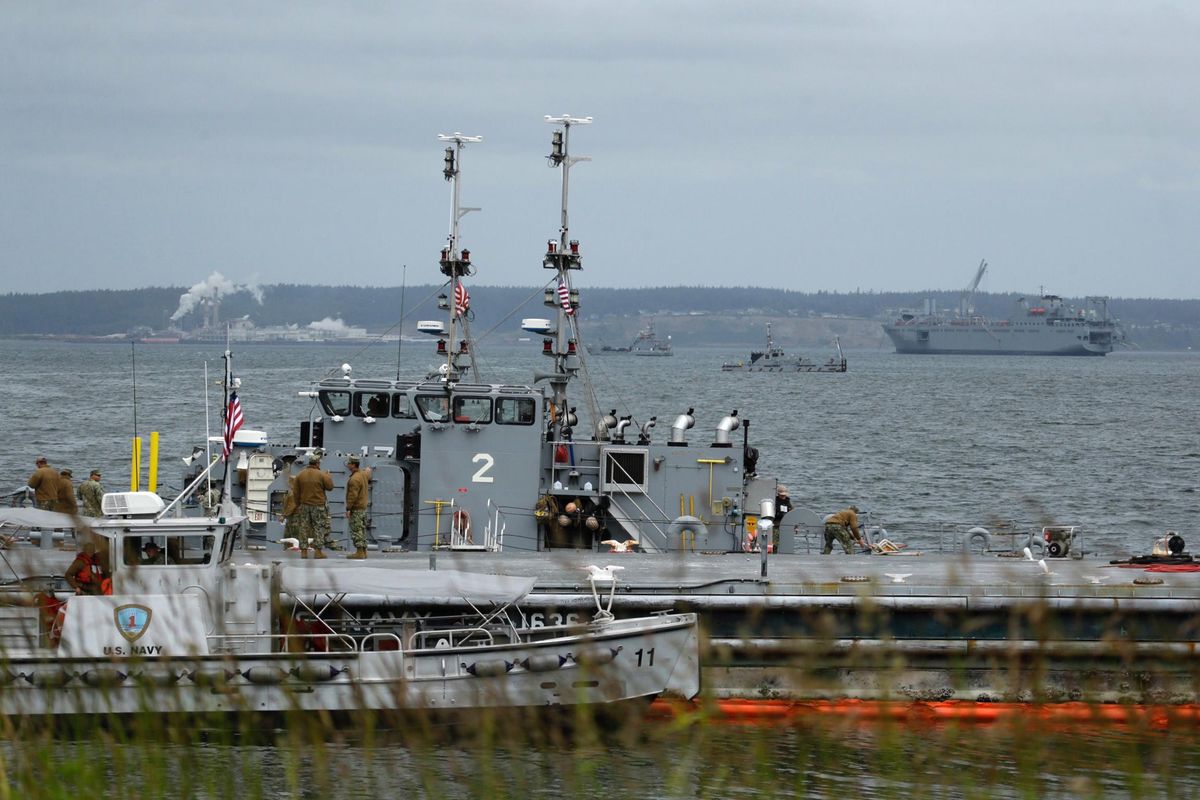 With the USNS Bob Hope cargo ship in the background, U.S. Navy sailors stand on the decks of boats used to bring cargo to the shore Wednesday on Naval Magazine Indian Island. (Ted S. Warren / Associated Press)