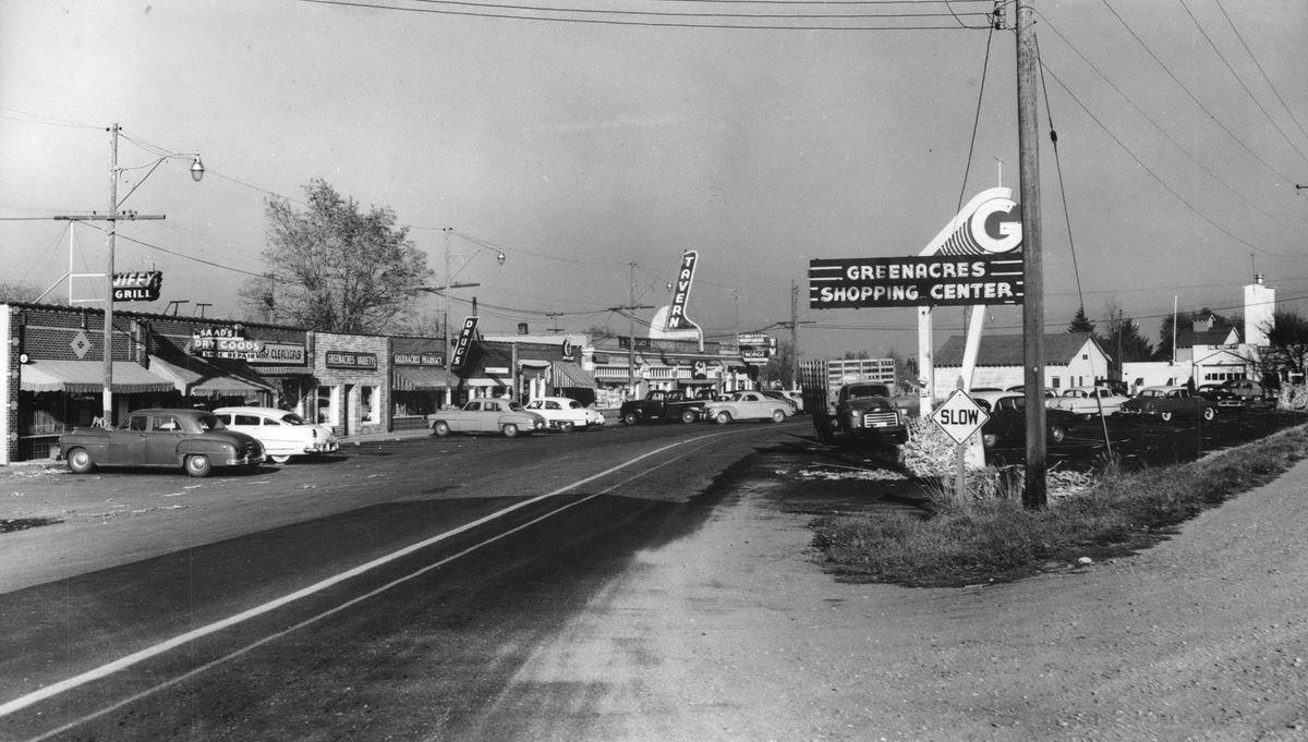 The Greenacres Shopping Center, a crescent of shops along East Appleway seen here in a 1954 photo, was a commercial center for the unincorporated agricultural community, which was founded started at the turn of the 20th century. The strip of shops date at least back to the 1920s, when a grocery store, later Greenacres IGA, was built there. Over the years, the center has included  a gas station, pharmacy, cafes and various stores. (SR)