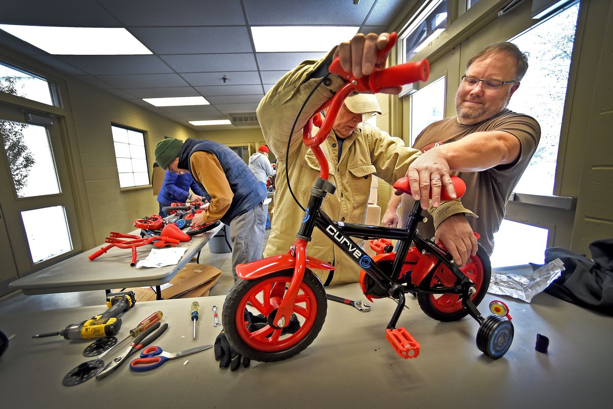 Paul Essex, center, and Patrick Morgan, right, team up Monday at the Christmas Bureau, following assembly directions and leaving no parts left over. At back left, John Rodgers tries to make sense of instructions as he starts on another bike.  (Christopher Anderson/For The Spokesman-Review)