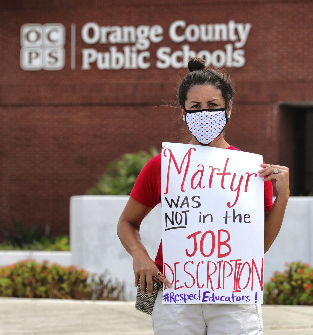 FILE - In this Tuesday, July 7, 2020 file photo, Rachel Bardes holds a sign in front of the Orange County Public Schools headquarters as teachers protest with a car parade around the administration center in downtown Orlando, Fla. As pressure mounts for teachers to return to their classrooms this fall, concerns about the pandemic are pushing many toward alternatives, including career changes, as some mobilize to delay school reopenings in areas hardest hit by the coronavirus. Teachers unions have begun pushing back on what they see as unnecessarily aggressive timetables for reopening.  (Joe Burbank)