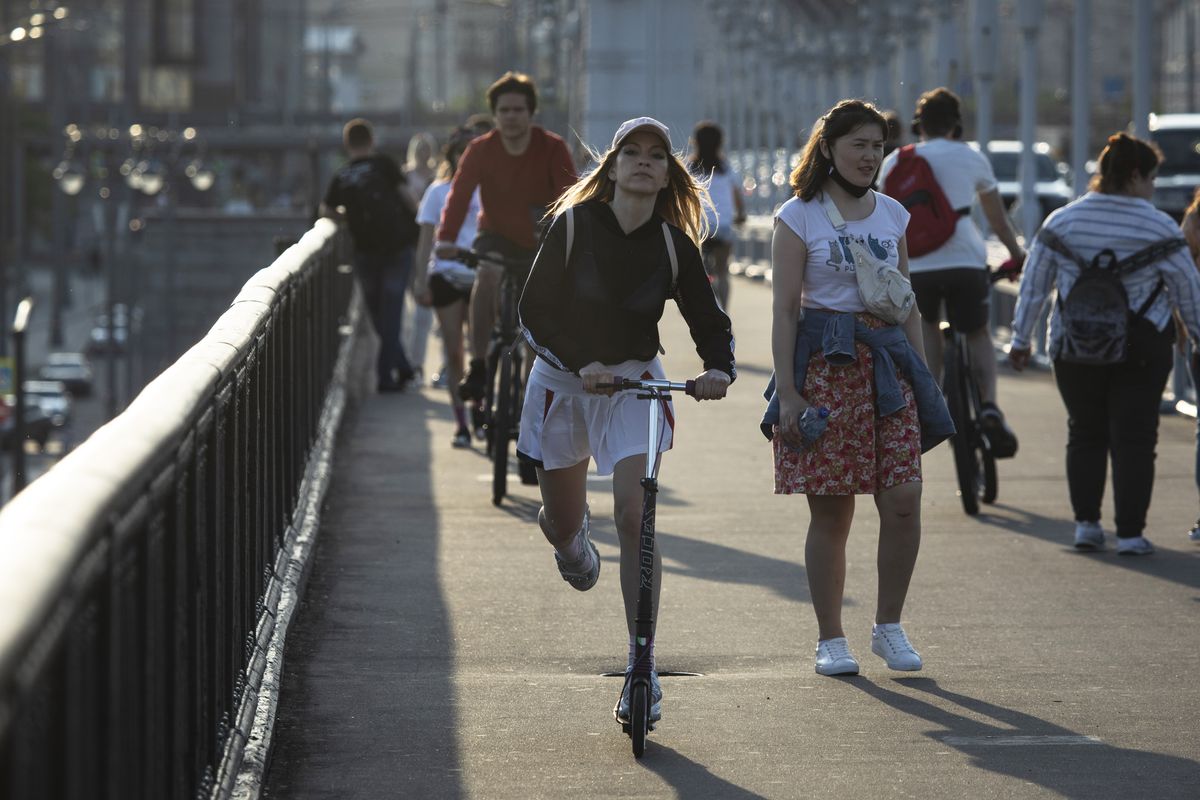 A woman rides a scooter as people cross the Krymsky Bridge in Moscow, Russia, Monday, June 8, 2020. The Russian capital is ending a tight lockdown that has been in place for more than two months, citing a slowdown in the coronavirus outbreak. Moscow