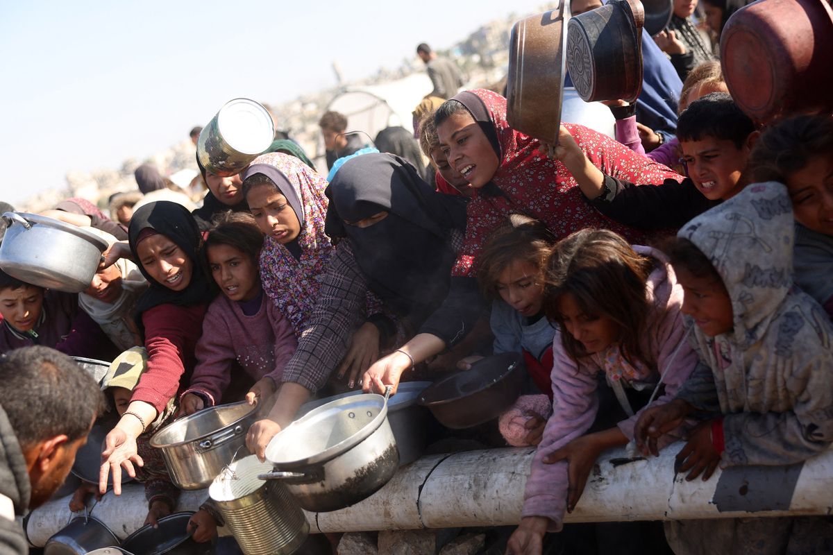 Palestinians stand in wait for a food portion at a distribution center south of Khan Yunis on Tuesday in the southern Gaza Strip.  (Bashar Taleb/AFP/Getty Images/TNS)