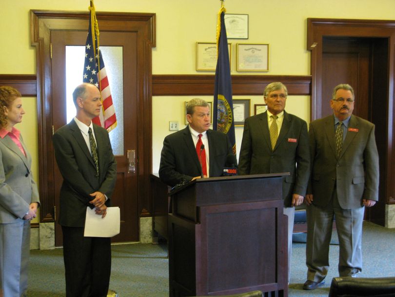 Idaho Attorney General Lawrence Wasden, at podium, speaks at news conference on drug pricing settlements Tuesday in Boise; at left is his consumer protection chief, Brett DeLange, and at right is Idaho Health & Welfare Director Dick Armstrong. (Betsy Russell)