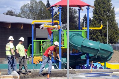 Workers for Cameron Reilly Concrete Contractors spread gravel around the children’s play structure at the Shadle Park pool Friday.  City officials believe they can open some pools as soon as late June,  much sooner than expected.  (Jesse Tinsley / The Spokesman-Review)