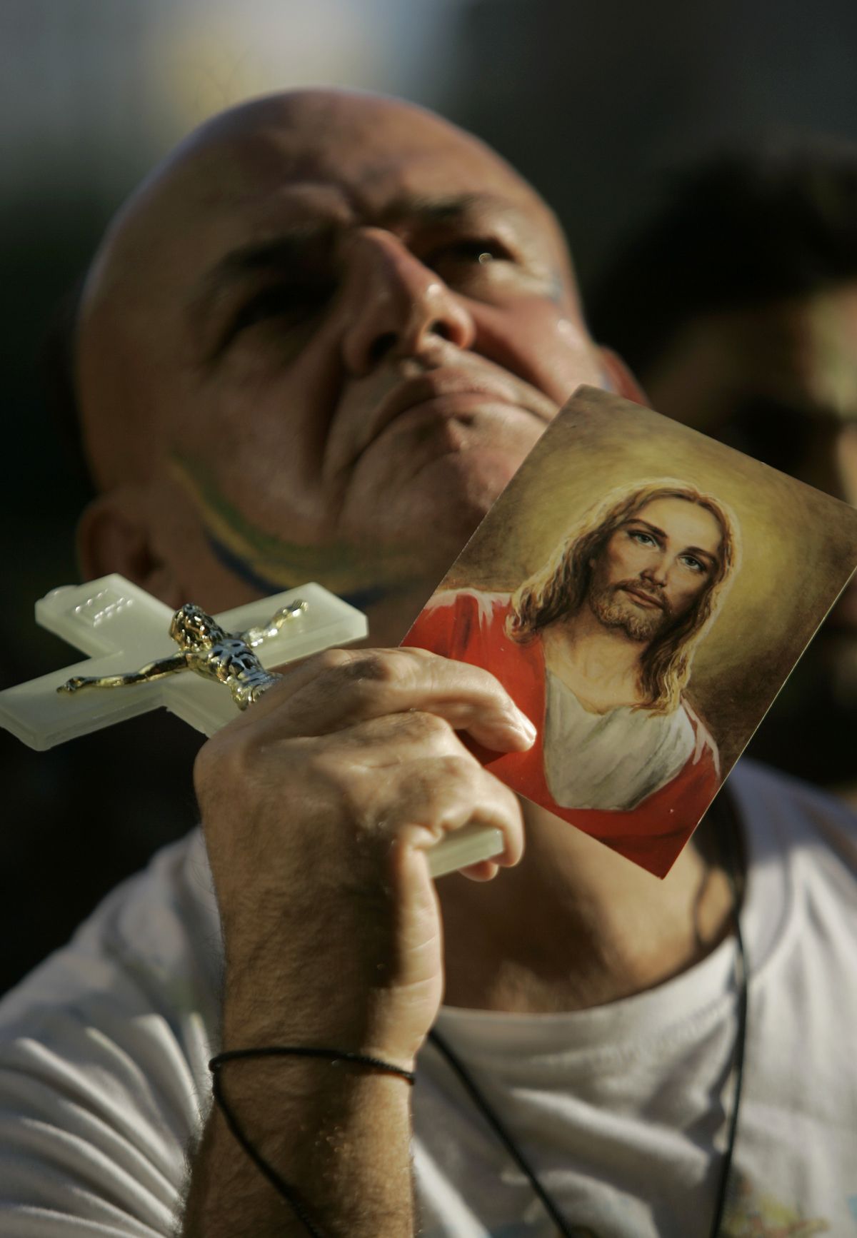 A Brazilian fan holds up a cross and an image of Jesus while watching the South Africa World Cup soccer match between Brazil vs North Korea on a giant screen, at Sao Paulo