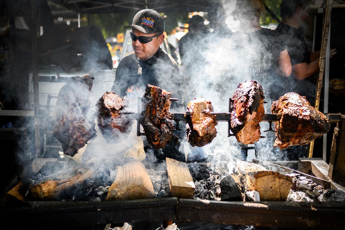 Jesus Andrade with Piggly’s BBQ, adds mesquite charcoal under roast beef rotating on a spit Wednesday  during the first day of Pig Out in the Park in Spokane’s Riverfront Park. (Colin Mulvany / The Spokesman-Review)