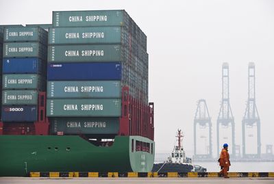 A worker walks past a cargo ship loaded with containers at the port in Tianjin, China, in March.  (Associated Press / The Spokesman-Review)