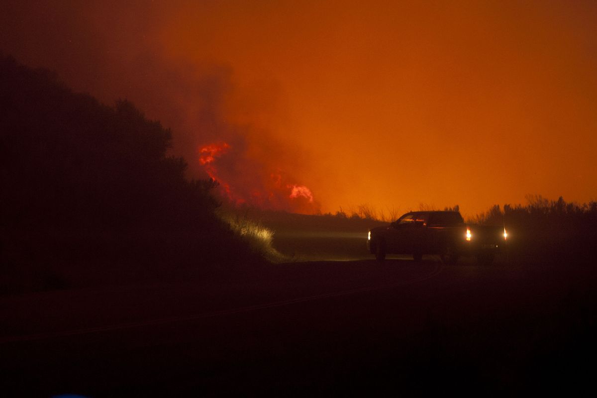 A pickup hangs a U-turn as flames jump the road Friday morning in Brewster.
