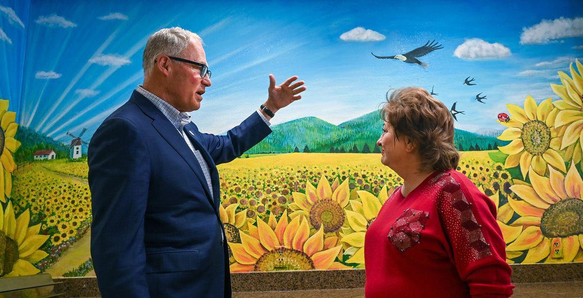 Gov. Jay Inslee talks Wednesday with artist Yelyzaveta Shchukina about her mural of sunflowers and Mount Spokane on the wall at the Thrive Center. Inslee toured the Spokane facility and had lunch with many refugees.  (DAN PELLE/THE SPOKESMAN-REVIEW)