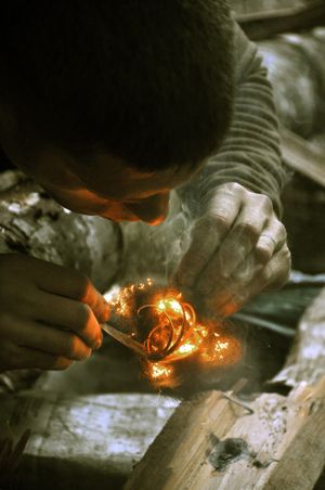 A "feather stick" can be the key to starting a fire in wet conditions. In this demonstration, Survival School instructor Nick Weber blows on the embers of steel wool tinder to ignite a feather stick he created with a knife by shaving curly strands of dry wood. Next he would add more feather sticks and kindling to build a fire on a platform of small logs. (Rich Landers)