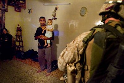 
An Iraqi man holds his child while U.S. Marines search his house in Fallujah on Wednesday. A suicide bomber blew himself up while standing in a line of police recruits that morning. 
 (Associated Press / The Spokesman-Review)