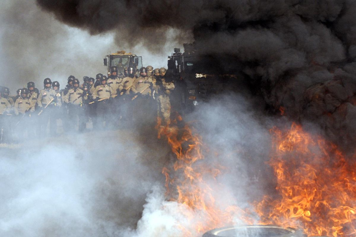 Law enforcement stand in the distance as fire and thick smoke from burning tires billows in the air as a Dakota Access Pipeline protester started the fire at a protest roadblock across Highway 1806 at the Front Line Camp in Morton County, N.D., Thursday, Oct. 27, 2016. (Mike McCleary / The Bismarck Tribune via AP)