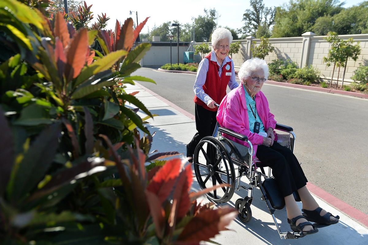 Pedal Pushers volunteer Anne Mose, 90, left, who is legally blind, visits with resident Flora “Flo” Burgess, 92, while pushing her wheelchair during a walk around campus at the Terraces at San Joaquin Gardens in Fresno. Pedal Pushers is a group of volunteers at the senior living campus who lead less-mobile neighbors on walks. (Silvia Flores / Tribune News Service)