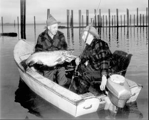 Wes Hamlet of Coeur d'Alene, Idaho, hoists the 37-pound world record rainbow trout he caught in Lake Pend Oreille on Nov. 25,1947. Hamlet is in the leaky wooden boat he was fishing in with partner Tony Moen, also of Coeur d'Alene. (Ross Hall)