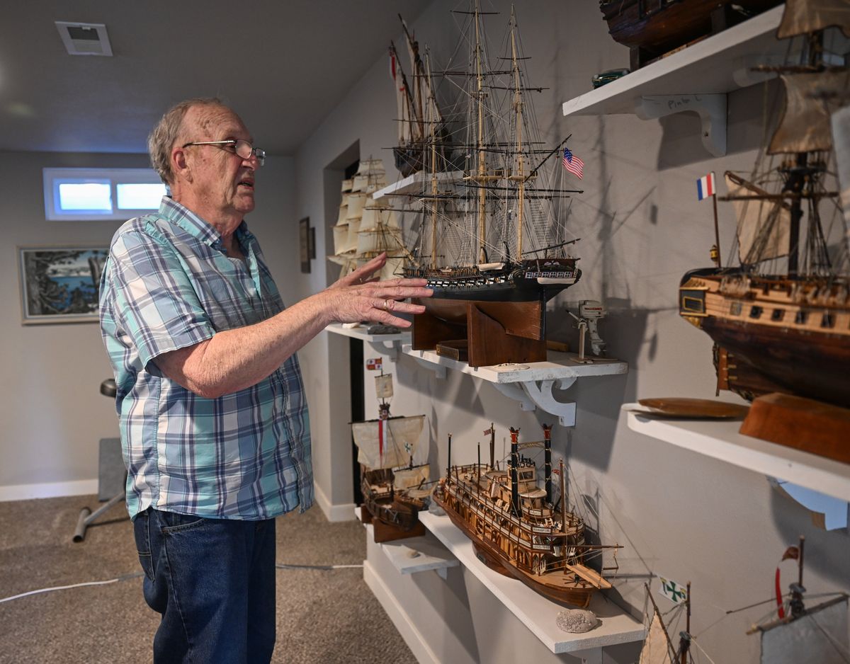 Bill Widrig stands next to the wall of ship models he has built where he displays them in the basement of his northside home, shown Thursday, Mar. 28, 2024. He is standing in front of a detail model of the U.S.S. Constitution. That model is plastic but many of his finished models are made of wood from detailed kits.  (Jesse Tinsley/THE SPOKESMAN-REVIEW)