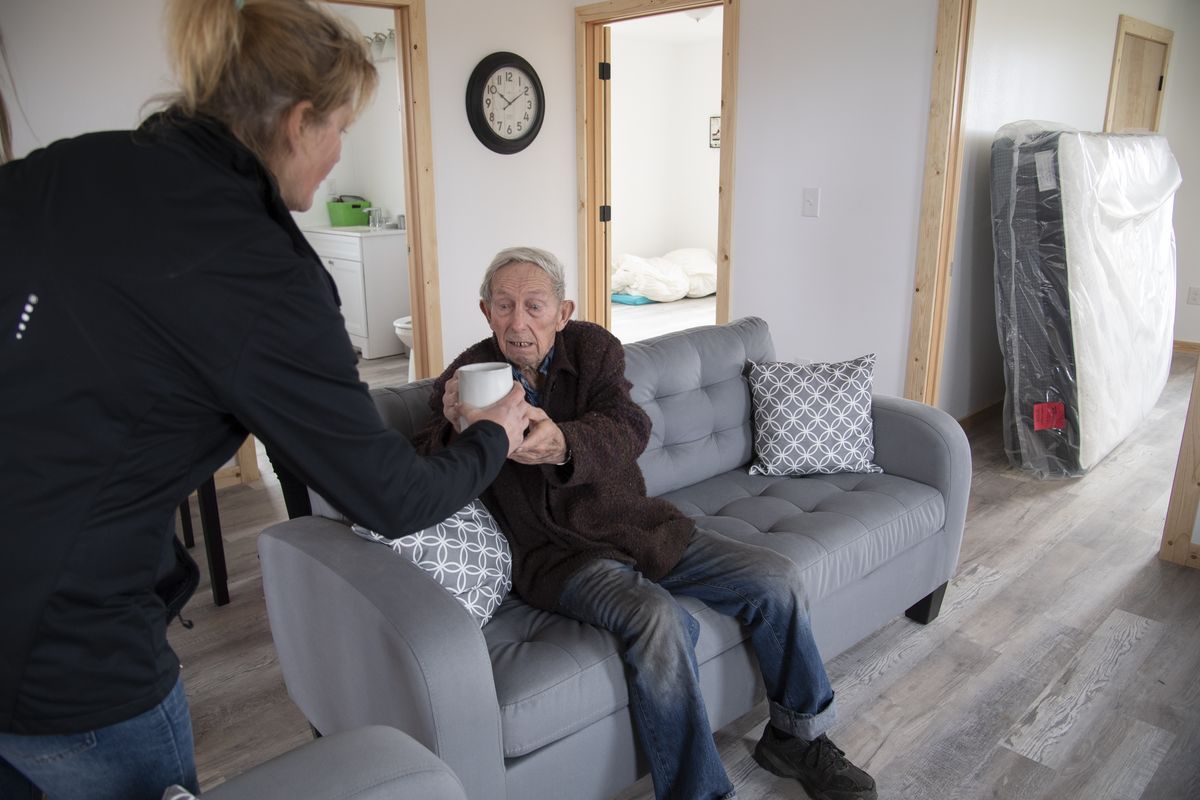 Diana Totten, left, hands a cup of coffee to Jim Jacobs, 90, a neighbor, after moving into the new home built for her and her daughter in Malden, Washington Friday, Mar. 26, 2021. The new home was just completed my missionaries of an Anabaptist community from Montana. A Spokane furniture store had just dropped off a couch set, a dining room set and a new mattress as a gift.  (Jesse Tinsley/The Spokesman-Review)