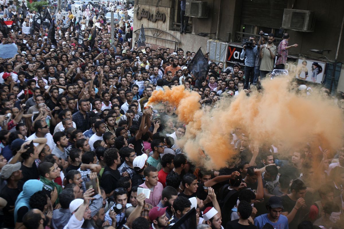 Protesters chant slogans amid orange smoke outside the U.S. embassy in Cairo, Egypt, Tuesday, Sept. 11, 2012. Egyptian protesters, largely ultra conservative Islamists, have climbed the walls of the U.S. embassy in Cairo, went into the courtyard and brought down the flag, replacing it with a black flag with Islamic inscription, in protest of a film deemed offensive of Islam. (Mohammed Zaid / Associated Press)