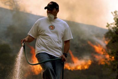 
Homeowner Mike Rosales sprays water on the roof of his house as flames make their way down a hillside in Simi Valley, Calif., Thursday.  
 (Associated Press / The Spokesman-Review)