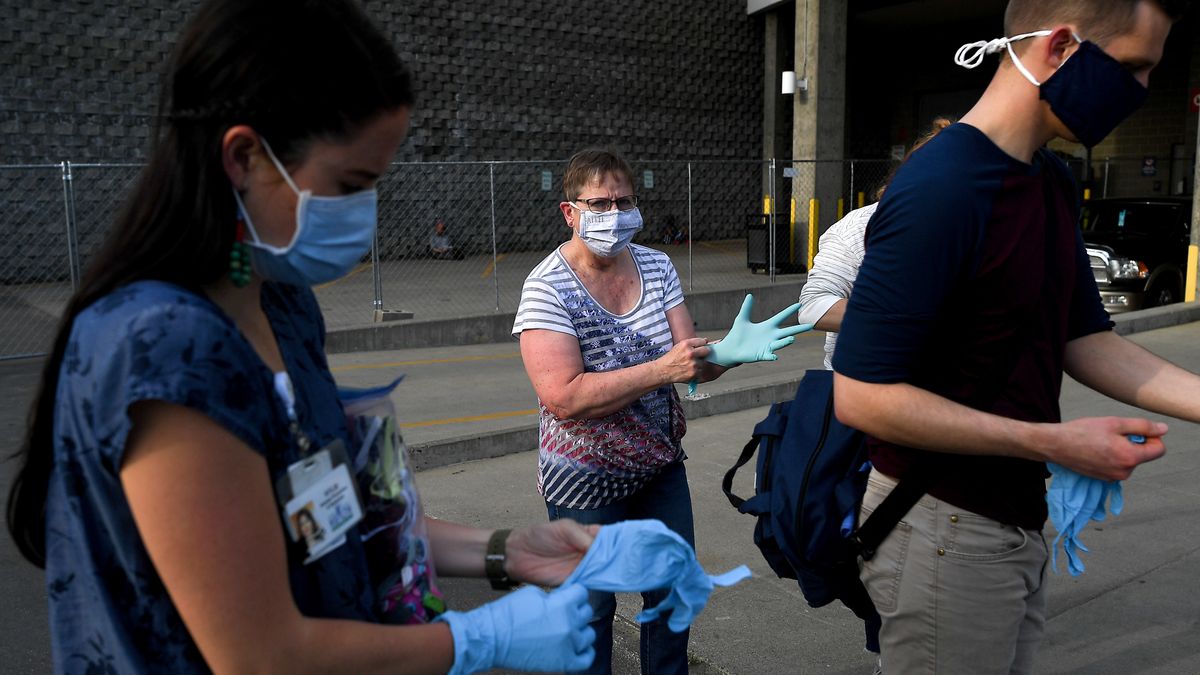 Volunteer Barb Warton, center, pulls on latex gloves as she joins Kylie Kingsbury, left, Homeless Outreach Coordinator with the Spokane Regional Health District and volunteer Brent Conrad, right, in preparing before doing COVID-19 screenings for the homeless on Thursday, May 28, 2020, at Spokane Arena.  (TYLER TJOMSLAND)