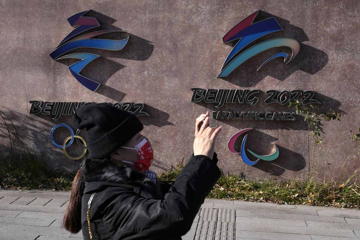 A woman wearing takes photos near the logos for the Beijing Winter Olympics and Paralympics in Beijing, China, Tuesday, Nov. 9, 2021. China on Tuesday, Dec. 7, 2021 accused the United States of violating the Olympic spirit by announcing an American diplomatic boycott of February