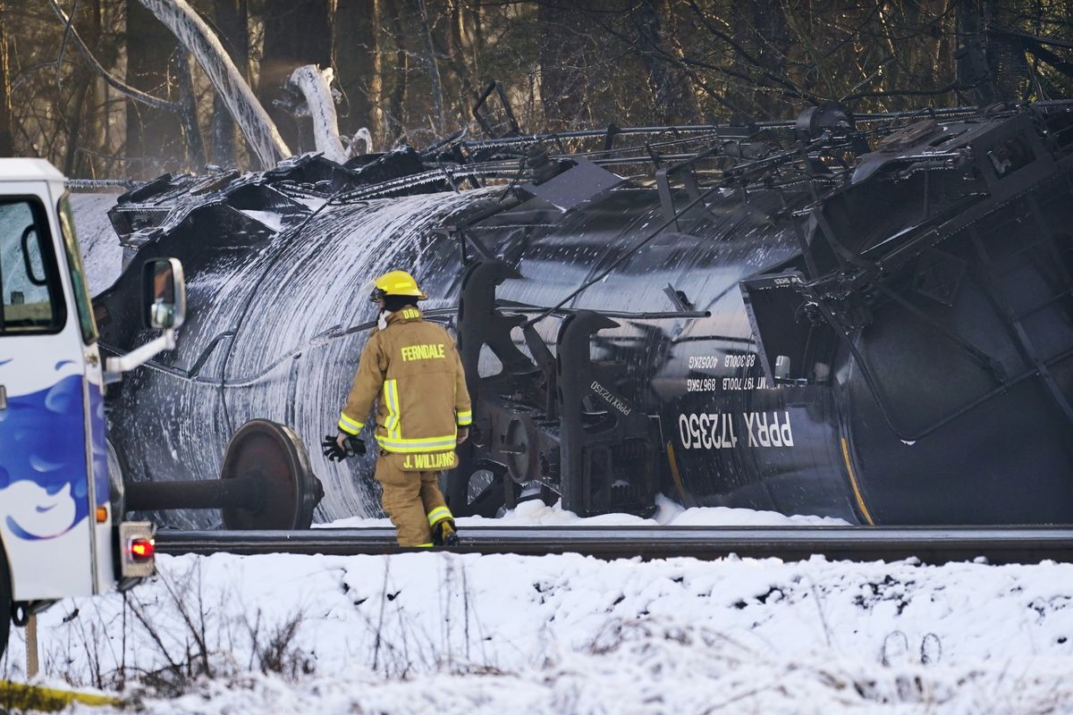 A firefighter walks past a derailed train car Tuesday, Dec. 22, 2020, in Custer, Wash. Officials say seven train cars carrying crude oil derailed and five caught fire north of Seattle and close to the Canadian border. Whatcom County officials said the derailment occurred in the downtown Custer area, where streets were closed and evacuations ordered during a large fire response.  (Elaine Thompson)