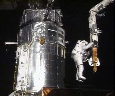 Astronaut John Grunsfeld, with the Hubble Space Telescope at his back, holds onto the shuttle’s robotic arm while working on repairs  Monday.  (Associated Press / The Spokesman-Review)