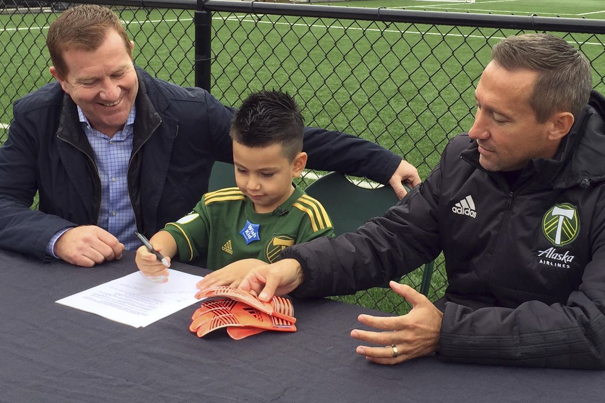 Five-year-old Derrick Tellez, center, signs his contract with Portland Timbers general manager Gavin Wilkinson, left, and coach Caleb Porter, right, on Friday, Sept. 22, 2017, at the Timbers practice facility in Beaverton, Ore. Tellez, who has had three surgeries for a cancerous brain tumor, was signed to a one-game contract with the MLS soccer team, granting his wish with Make-A-Wish Foundation Oregon. (Anne M. Peterson / Associated Press)
